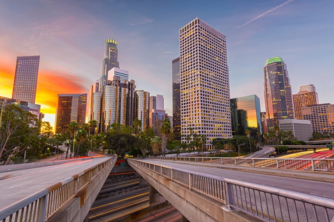 Sunset view of downtown Los Angeles with modern skyscrapers, palm trees, and light trails on city highways
